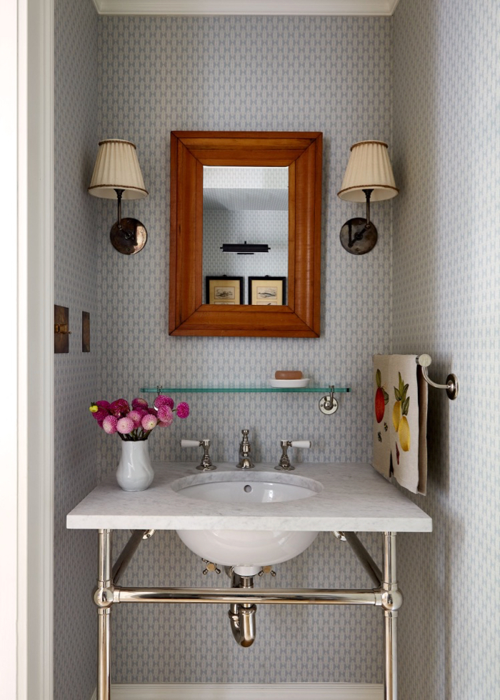 Powder room with wallpaper and sconces. Chrome vanity with marble counter. Glass shelf. Decorated by McGrath II.