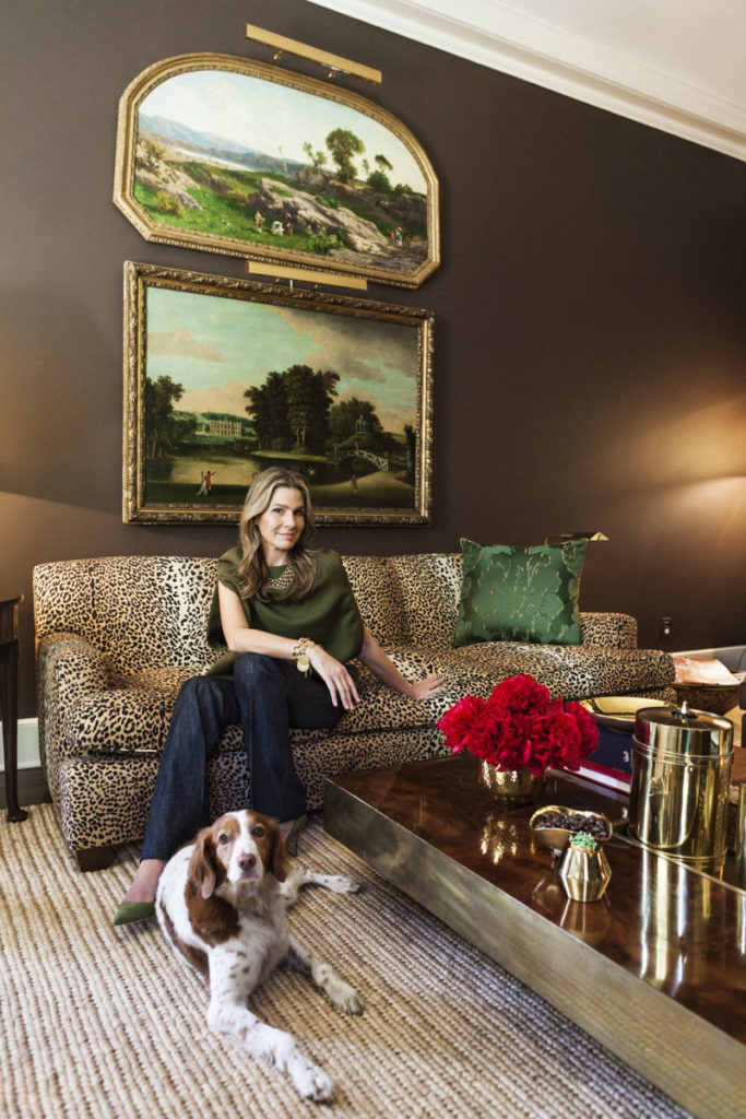 Aerin Lauder at home in her East Hampton living room on a leopard print sofa. Chocolate brown painted walls.