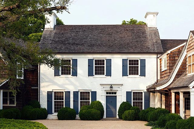 White brick house with navy blue shutters and front door and pea gravel driveway. Hamptons, New York.